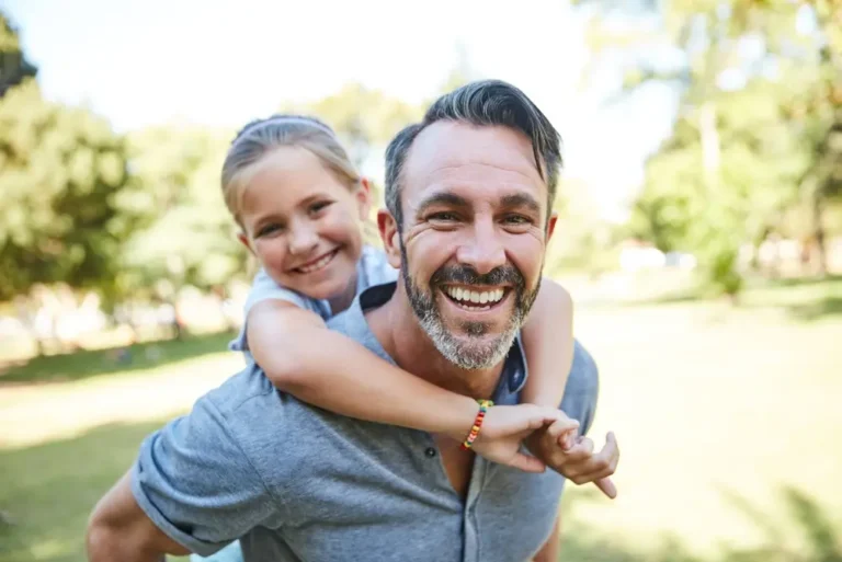 Father smiling, giving daughter a piggyback ride outside on a nice day