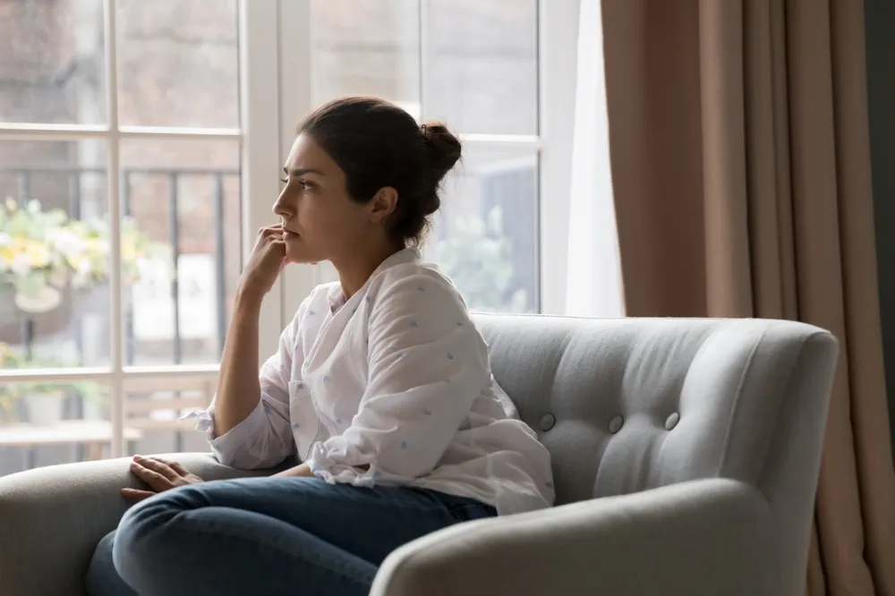 Sad woman sitting on the couch, staring out the window