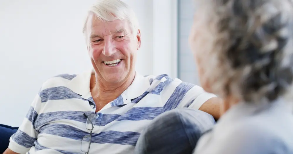 Senior man laughing on the couch, talking to spouse