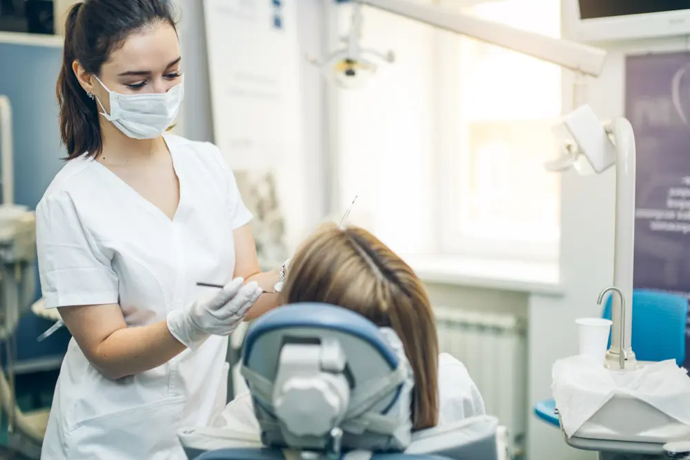 careful professional dentist in white uniform treating patient's teeth, making perfect smile for patients, using medical equipment
