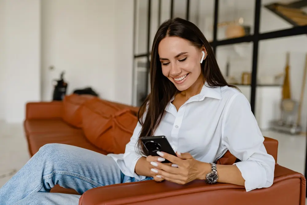 Happy, smiling woman looking down at her phone while she sits on her couch