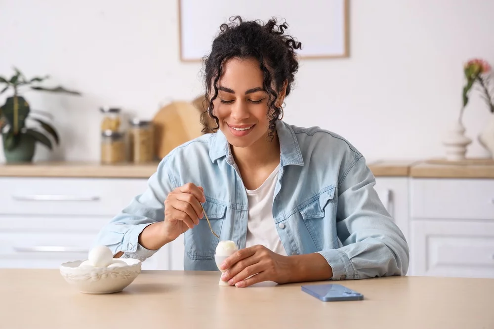 Young woman eating a hard boiled egg in the kitchen